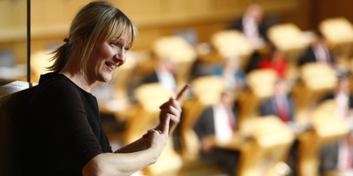 Woman speaking BSL in front of the Scottish Parliament Chamber